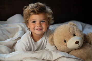 A young child in pristine pajamas enjoying morning play on the bed with a teddy bear.