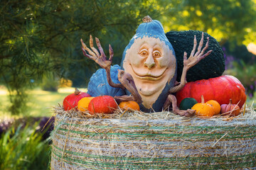 Funny carved pumpkin, with a happy smile sitting on a hay bale among other colorful pumpkins