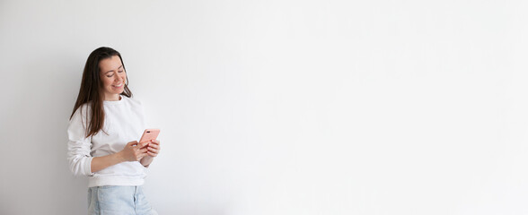 Young woman talking on mobile phone, smiling, using social media. Millennial person in white sweatshirt on white background. People using technology. Work call. Copy space right.