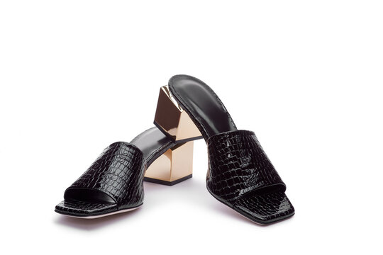 Bold black crocodile patent leather mules with metallic gold block square heels isolated on the white background. Concept of modern design summer shoes.