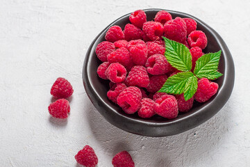 fresh raspberries, on a black plate, with leaves, top view, on a white table,
