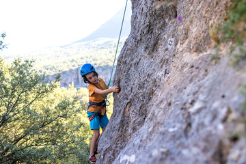 Children's rock climbing. The boy climbs a rock against the backdrop of mountains. Extreme hobby....