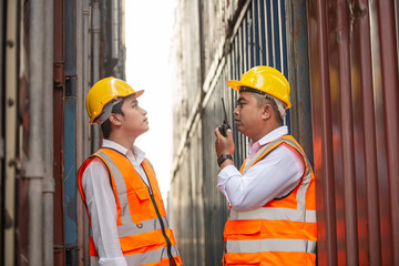 Asian logistic worker talking on walkie talkie to colleague at container warehouse for checking stock. Shipping export business concept