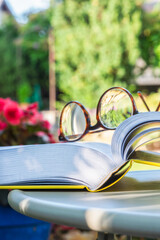Reading glasses and open book on table in summer garden