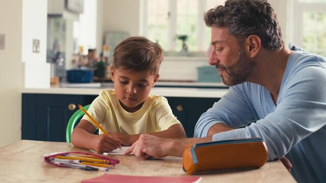Mature father in kitchen at home with son sitting at table helping with homework - shot in slow motion