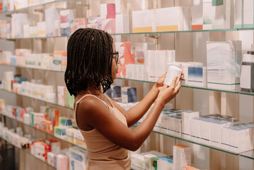 Black woman with dreadlocks reading label on bottle at pharmacy