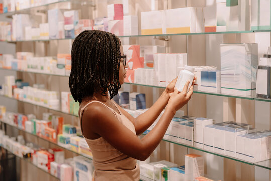 Black woman with dreadlocks reading label on bottle at pharmacy