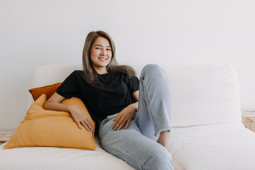 Fototapeta premium Happy asian woman sits and relax on sofa in one good fine day.