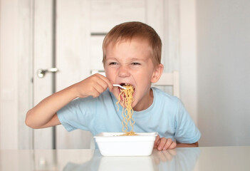 Happy preschool child eats spaghetti pasta. Boy in kitchen at table eating noodles. Concept of baby food. Enjoy your meal