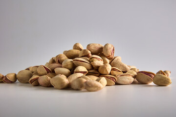 Salty delicious unpeeled pistachios close-up, an appetizing snack for beer. Small handful of nutritious pistachio nuts in a shell on a white background is laid out in a pile. 