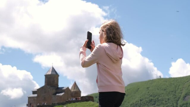 Little girl taking photos of old Georgian church in summer day, slow motion. World travel concept
