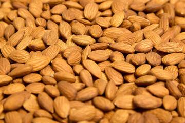 Close-up of delicious healthy almonds laid out in front of the camera, top view. Background of brown large raw peeled almonds, arranged randomly.