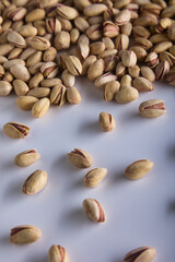 Unpeeled pistachio nuts are randomly scattered on a white background. Dried fried salty delicious pistachios in a shell, top view. 