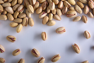 Dried fried salty delicious pistachios in a shell, top view. Unpeeled pistachio nuts are randomly scattered on a white background