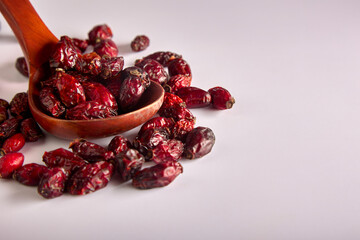 On a white background, a top view of a wooden spoon with large dry berries of healthy rosehip. Useful rosehip fruits are scattered on a white background