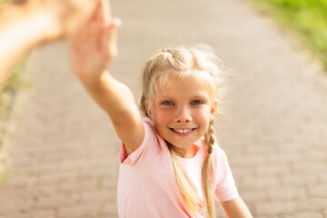 Pretty smiling schoolgirl giving high five while walking and riding bike in park, closeup