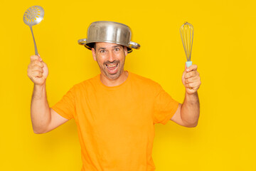 Funny bearded crazy hispanic man with a saucepan on his head and other kitchen utensils in his...