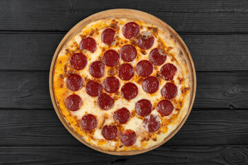 Top view of hot pepperoni pizza on black wooden background, flat lay.