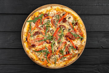 Freshly baked pizza with mozzarella cheese, salami, mushrooms, tomato sauce, olives, red peppers and parmesan on wooden background, top view