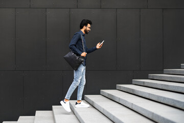 Young middle eastern guy entrepreneur going up stairs, using phone