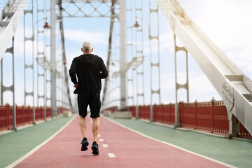 Back view senior sportsman jogging by city bridge, copy space