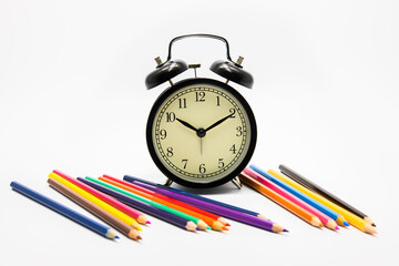 alarm clock with color pencils on yellow background
