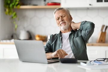 Tired Elderly Man Suffering Neck Pain After Working With Laptop At Home