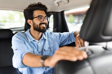 Happy young indian guy sitting inside car taxi and smiling