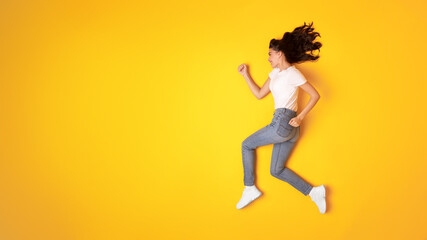 Fototapeta na wymiar Happy Lady Running In Mid Air Looking Aside, Yellow Background