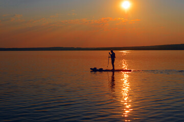 side view silhouette of alone male paddle boarder in sunset. Paddle-boarding in the bay. During sunset, one young man, paddleboarding with stand up paddle board on a lake.