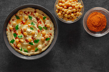 Hummus with oil and spices in bowl, on slate stone plate round, dark background, top view