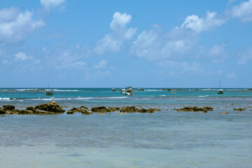 beach with blue sky, low tide, corals and boats in the background