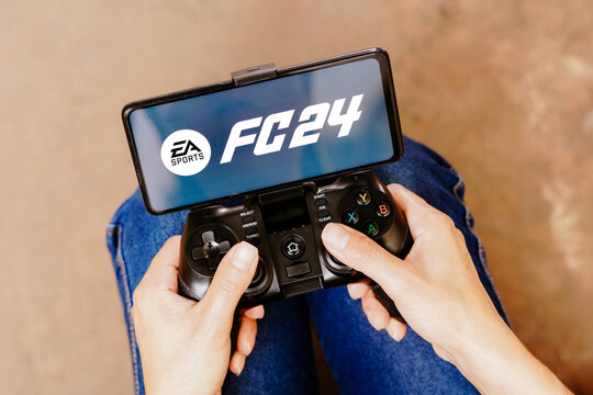 August 8, 2023, Brazil. In this photo illustration, a person playing on a joystick and the EA Sports FC 24 logo displayed on a smartphone screen.