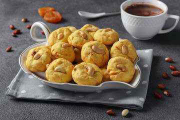Homemade carrot cookies with cashews, peanuts and dried apricots and a cup of coffee on a gray background
