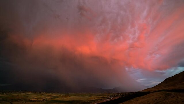 Timelapse of rainstorm at sunset as rainbow fades and lightning flashes as the clouds change vibrant colors over Utah.