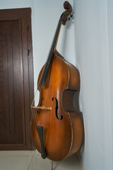 An old double bass leaning on a white wall.
