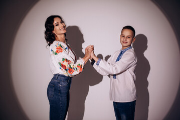 Happy mother and her son in Ukrainian national clothes on gray background