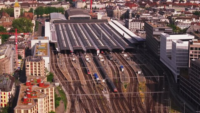 Aerial footage of Hauptbahnhof on sunny day. Roofed platforms, various passenger trains and surrounding buildings in city. Zurich, Switzerland