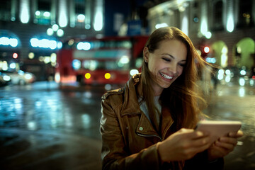 Young woman using a smart phone at night at the Piccadilly Circus in London