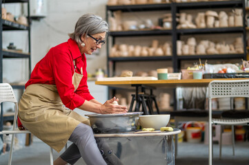Woman potter molding pot shape on pottery wheel at her workshop.