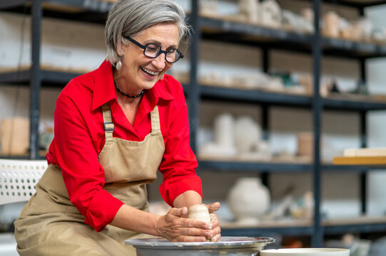 Woman working on potters wheel creating clay products at her workshop.