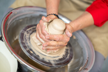 Woman working on potter's wheel in a pottery workshop, creating clay pot.