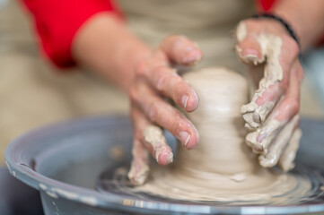 Woman working on potter's wheel in a pottery workshop, creating clay pot.