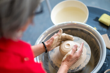 Fototapeta premium Woman working on potter's wheel in a pottery workshop, creating clay pot.