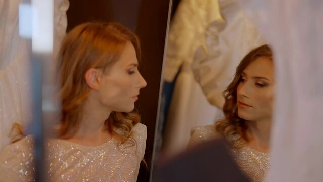 womanly gay man in wedding dress admiring his reflection in mirror in wedding atelier, portrait