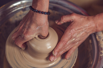 Woman working on pottery wheel and sculpting clay pot.