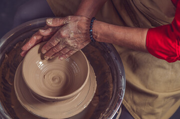 Hands of mature woman master of ceramics working on a potter's wheel, making plate of clay in art...