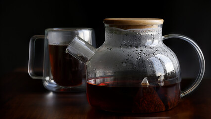Glass teapot with hot strong black tea, pyramid tea bags and double wall thermo mug on vintage wooden table. Tea drinking. Selective focus.