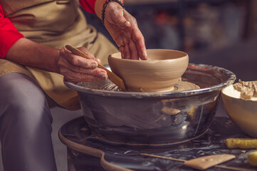 Female potter molding plate with hand tool, creating earthenware in workshop.