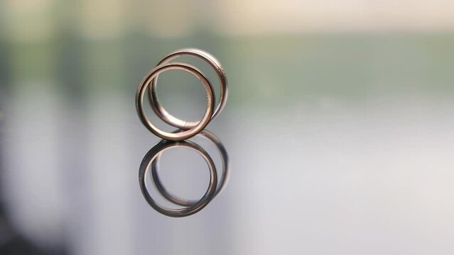 Wedding rings. A man's wedding ring rolls across the glass table to a woman's wedding ring.